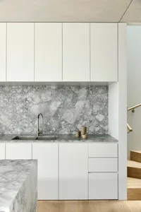 A minimalist kitchen with white cabinets and marble countertops.