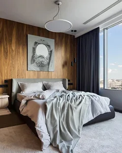 Modern bedroom with a walnut accent wall and fabric bed, featuring natural light from large window.