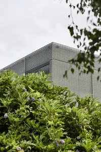 A modern building with a metallic frame and greenery in the foreground.