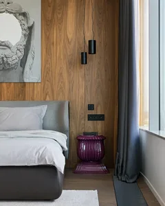 Modern minimalist bedroom featuring wooden walls, a grey upholstered bed, and a purple accent side table.