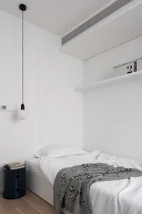 Minimalist bedroom featuring a bed with white bedding, a black accent lamp, and a wooden floor.