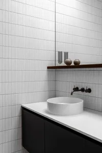 Modern minimalist bathroom with white tiled walls, black cabinets, and a white porcelain sink.