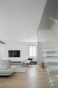 Modern minimalist living room with white furniture, wooden floors, and a glass staircase.