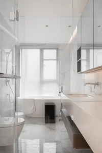 A modern bathroom with white marble tiles, a freestanding bathtub, a glass shower enclosure, and a minimalist design.