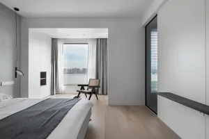 A modern bedroom with white walls, gray flooring, and a large window overlooking a cityscape.