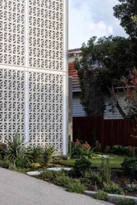 Modern residential garden with a geometric concrete wall and various green plants.