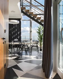 A modern dining room with black chairs around a table, large windows, and a geometric floor pattern.