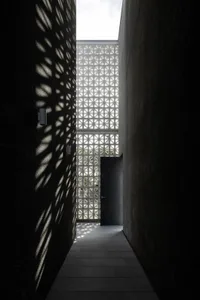 A corridor with concrete walls displaying geometric shadows created by a grid-like structure above.