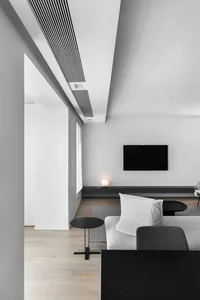 A modern minimalist living room with a white sofa, black coffee tables, and a television mounted on the wall.
