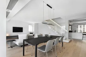Contemporary living room with minimalist design, featuring a white couch, grey chairs, and natural wood flooring.