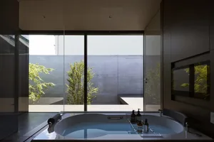 A clean, minimalist bathroom featuring a bathtub with a glass wall, concrete walls, and porcelain tiling.