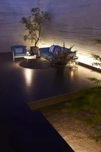 Outdoor lounge area with modern furniture, potted plants, and illuminated space against a concrete wall.