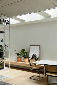 A minimalist living space featuring wooden flooring, white brick walls, concrete ceiling, and metal furniture.
