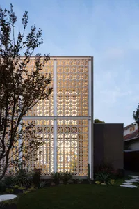 A modern concrete exterior with a grid of light fixtures and surrounding plants at dusk.