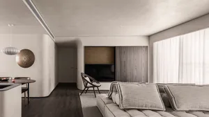 A minimalist living room with a large sectional sofa, a wooden armchair, and a dining area with a round table and chairs.