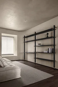 Modern living room with concrete walls, metal shelving, and a plush off-white couch on a gray rug.