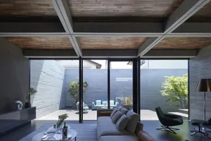 A modern concrete living room featuring a cozy sofa, stylish furniture, and large windows overlooking a serene courtyard.