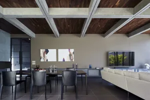 A modern concrete living room with a large sectional sofa and a dining area with black chairs and a table.