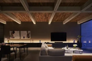A modern living room with concrete walls and wooden ceiling beams, featuring a cozy sectional sofa and a sleek dining table w