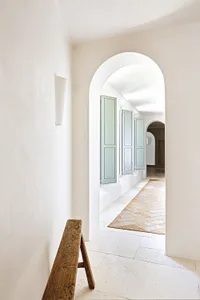 A minimalist hallway with white walls, wooden bench, and blue shutters.