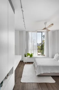A modern minimalist bedroom featuring white furniture and a wooden floor.