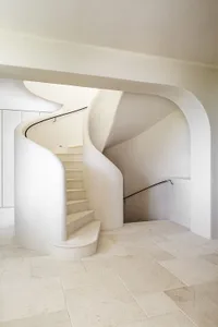 A modern, white stone staircase with curved walls and railings.