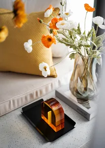 A close-up of orange and white flowers arranged in a glass vase on a terrazzo table next to a book titled 'Moment'.
