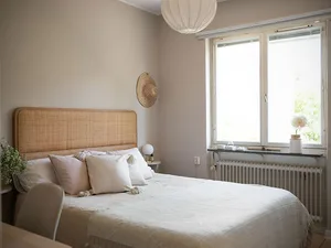 A minimalist bedroom with a white bedspread, wooden bed frame, and a window letting in natural light.