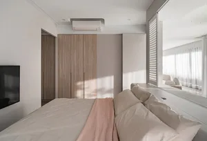 A minimalist bedroom with a large wooden wardrobe, a soft beige bed, and a pink throw blanket.