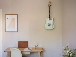 A minimalist home office featuring a wooden desk, a white chair, a brown leather bag, a candle holder, and a framed abstract 