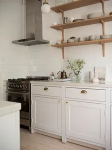A minimalist kitchen with white shelves, wooden cabinets, and a stainless steel stove.