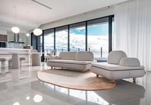 Modern minimalist living room featuring a fabric sofa with a round rug and floor-to-ceiling windows overlooking a scenic land