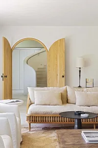 Minimalist-style living room with a wooden sofa, wooden coffee table, and white accent chairs, featuring a wooden-framed door