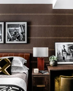 A modern bedroom featuring a brown leather headboard, wooden nightstand, framed photos, and a green plant.