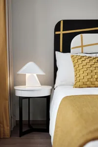A modern bedroom featuring a bed with a black and white patterned headboard, a white lamp, and a woven yellow throw pillow.