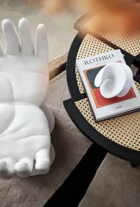 A modern ceramic sculpture of a hand on a wooden table next to a book with a white abstract sculpture on top.