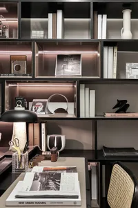 A modern home office with black furniture and white walls, featuring a desk, shelves with books, a desk lamp, and decorative 