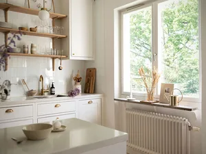 A modern kitchen featuring white walls, wooden shelves, and a white countertop with kitchen utensils and a bowl of fruit.
