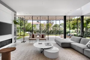 Modern living room with glass walls and concrete flooring, featuring a comfortable seating area and a minimalist aesthetic.