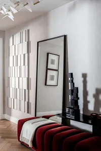 A modern living space featuring a red upholstered bench with a white throw blanket, a tall black mirror, and abstract white d