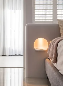 A minimalist bedroom with a soft, ambient light from a circular wall lamp made of light-colored wood.