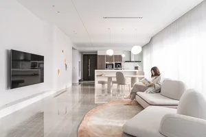 A modern interior living space with neutral tones, featuring a large sofa, a coffee table, a TV, and a dining area in the bac