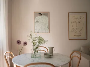 A modern residential dining space featuring a round table with a marble surface, wooden chairs, and framed artworks on the wa