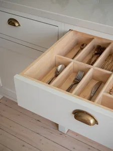 Organized wooden drawer with slotted compartments for cutlery in a modern white kitchen