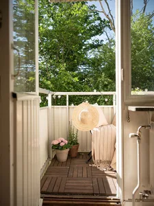 A small balcony features a wooden deck, potted plants, and a cozy sitting area with a beige cushion and throw blanket.