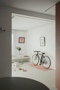 A minimalist home interior featuring a bicycle on a yoga mat, a small table with a vase, and framed pictures on the wall.