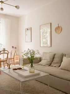 A modern minimalist living room with a beige sofa, white walls, and neutral-toned decor.