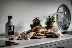 A modern kitchen with a wooden countertop, bread loaf, and potted plants on the counter.
