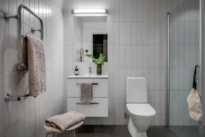 A modern minimalist bathroom with white tiled walls, a white toilet, and a white vanity with a sink.