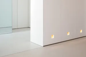 A modern minimalist white paneling storage unit with integrated lighting in a minimalistic interior space.